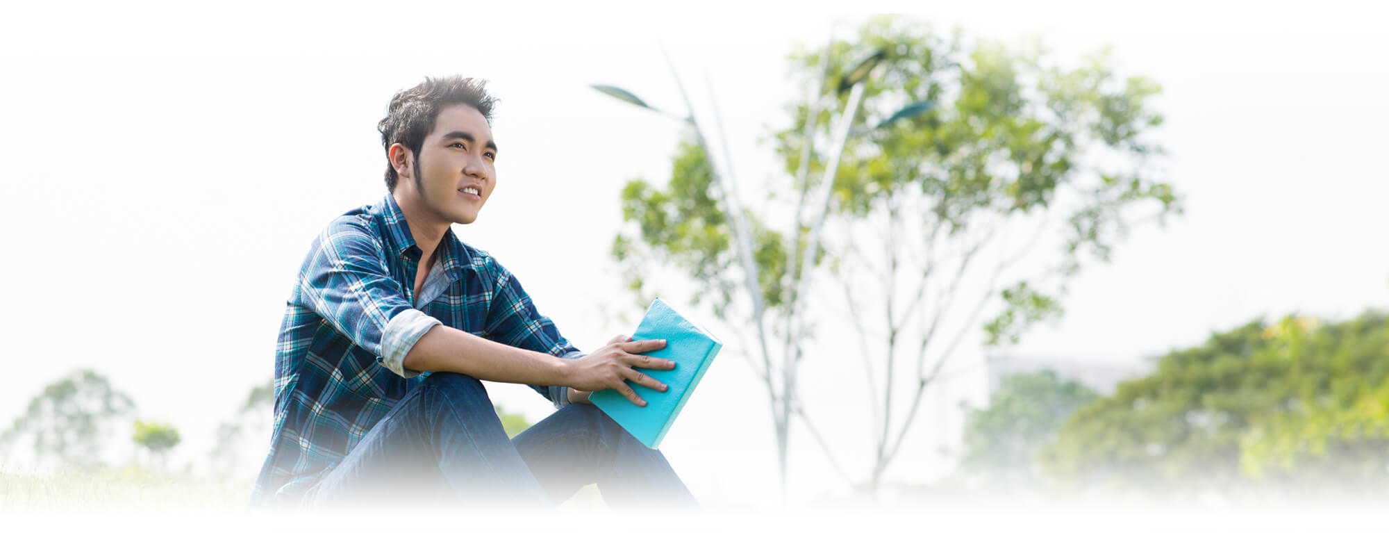 high school boy sitting on ground holding book