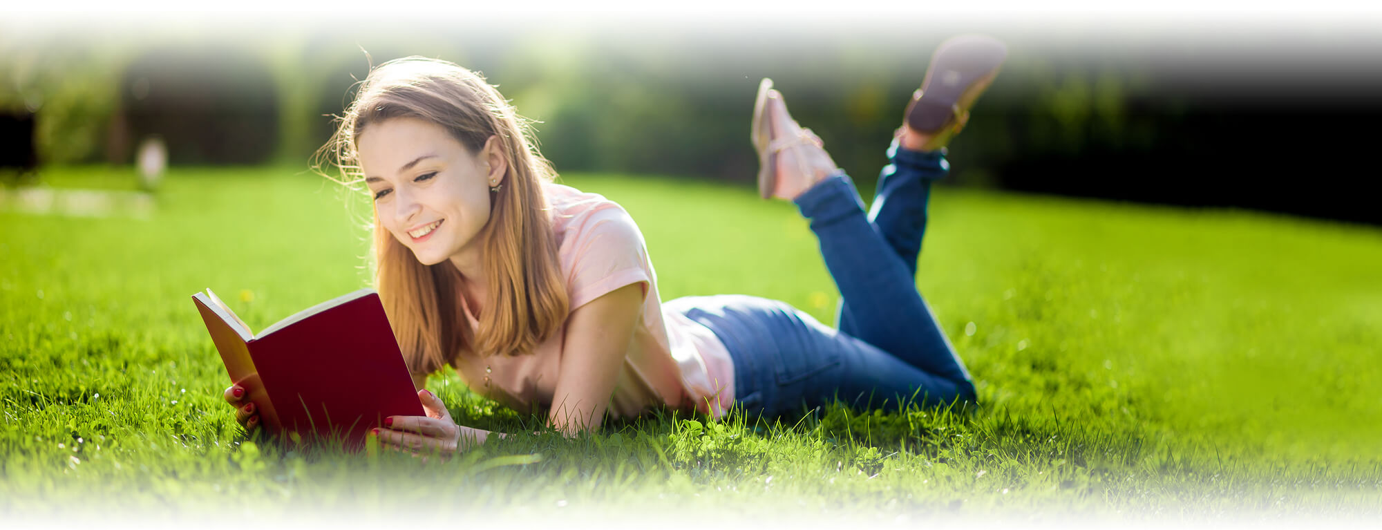 high school girl lying in field reading book