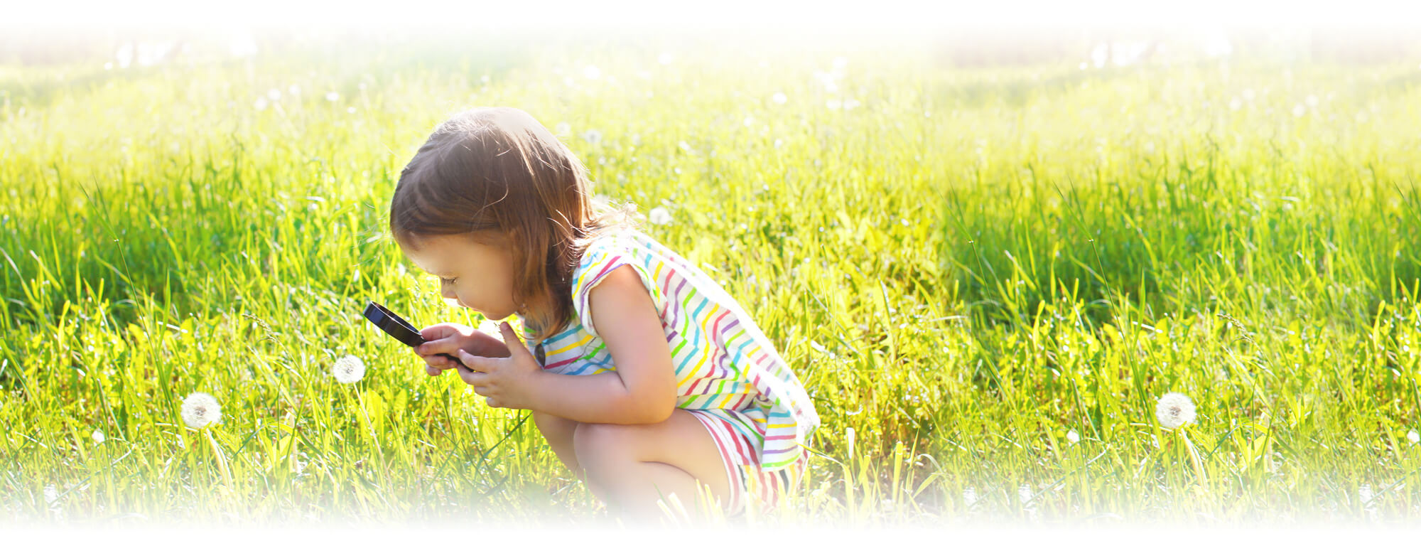 Prek girl in field with magnifying glass
