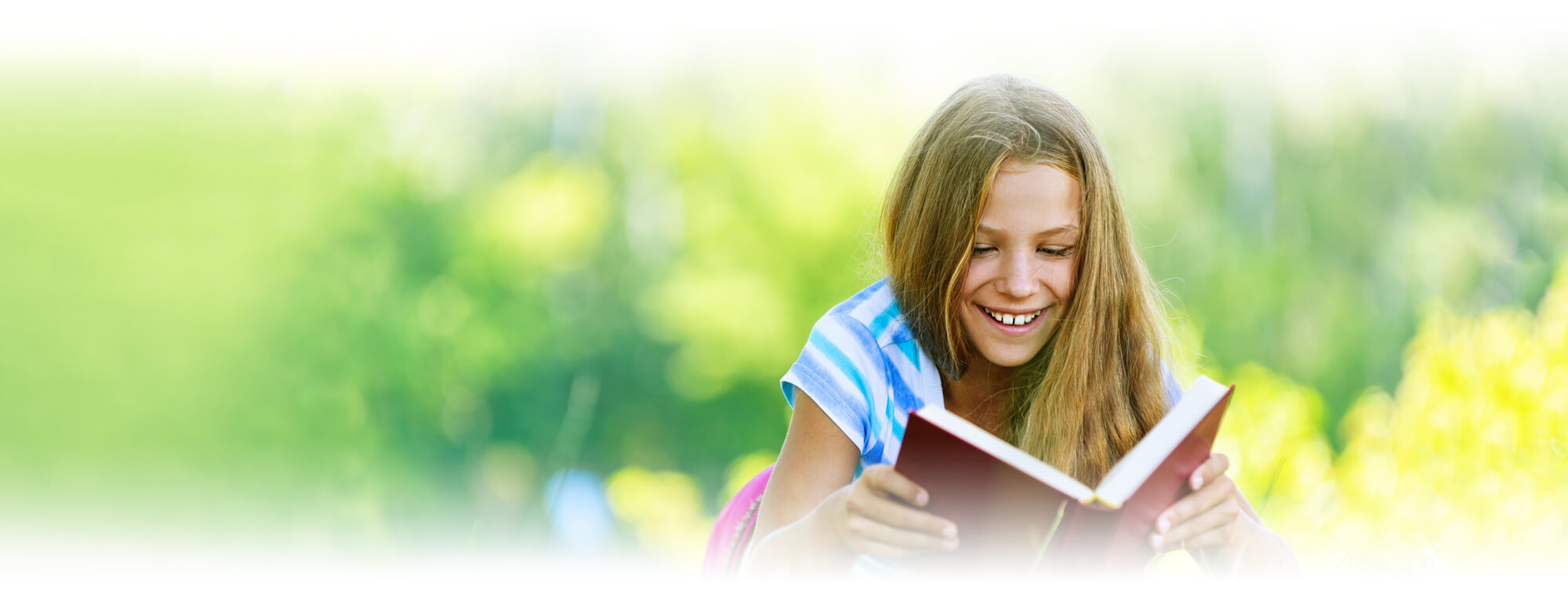 student girl lying on grass reading book