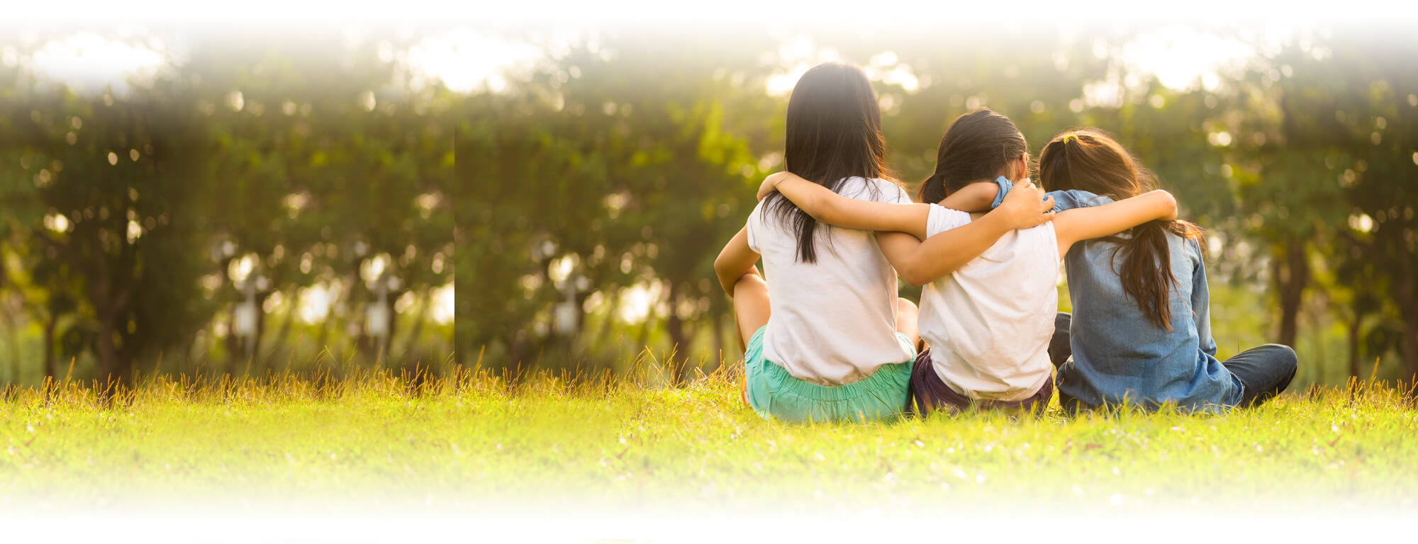 three student girls sitting on grass with arms around each other